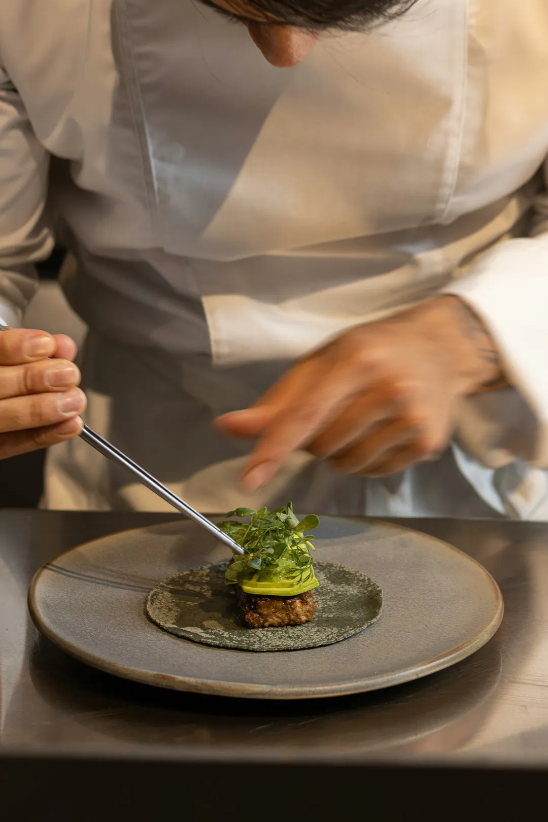 Küchenchef richtet ein Gericht mit Kräutern präzise mit der Pinzette an